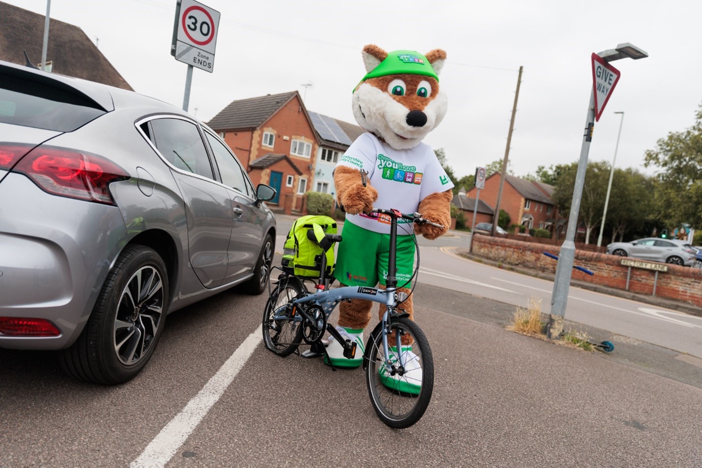 Theo the Fox, the Choose How You Move mascot, poses with a bicycle in a car park for a back to school active travel photoshoot