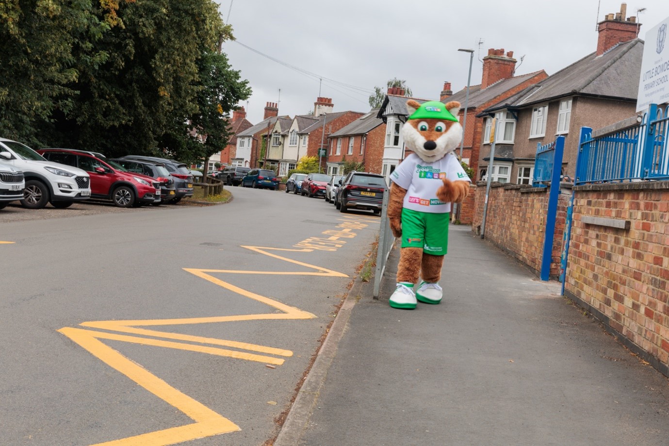 Choose How You Move's fox mascot walking on a path next to a school and zig zag lines